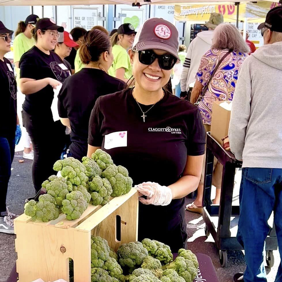 A woman standing next to broccoli at an outdoor market.
