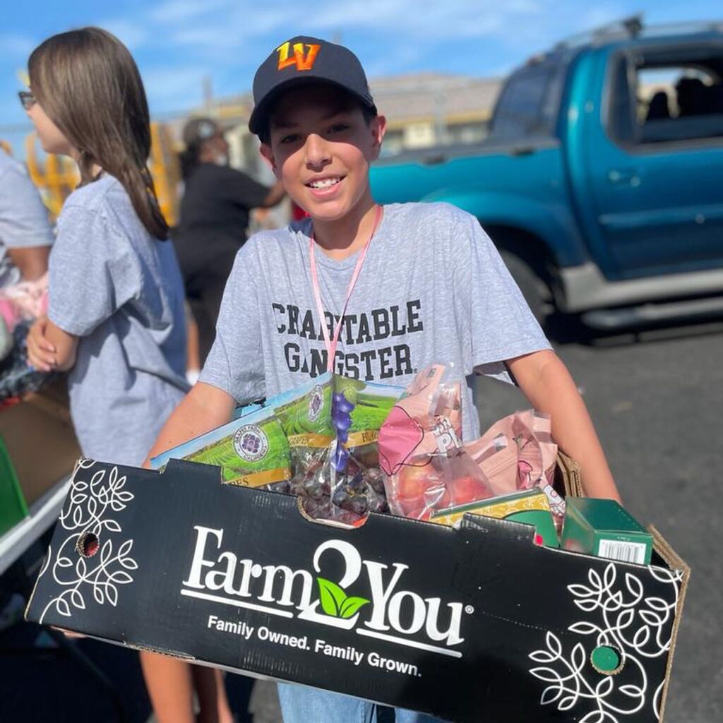 Image of a young volunteer carrying produce at The Just One Project's Farmers Market.
