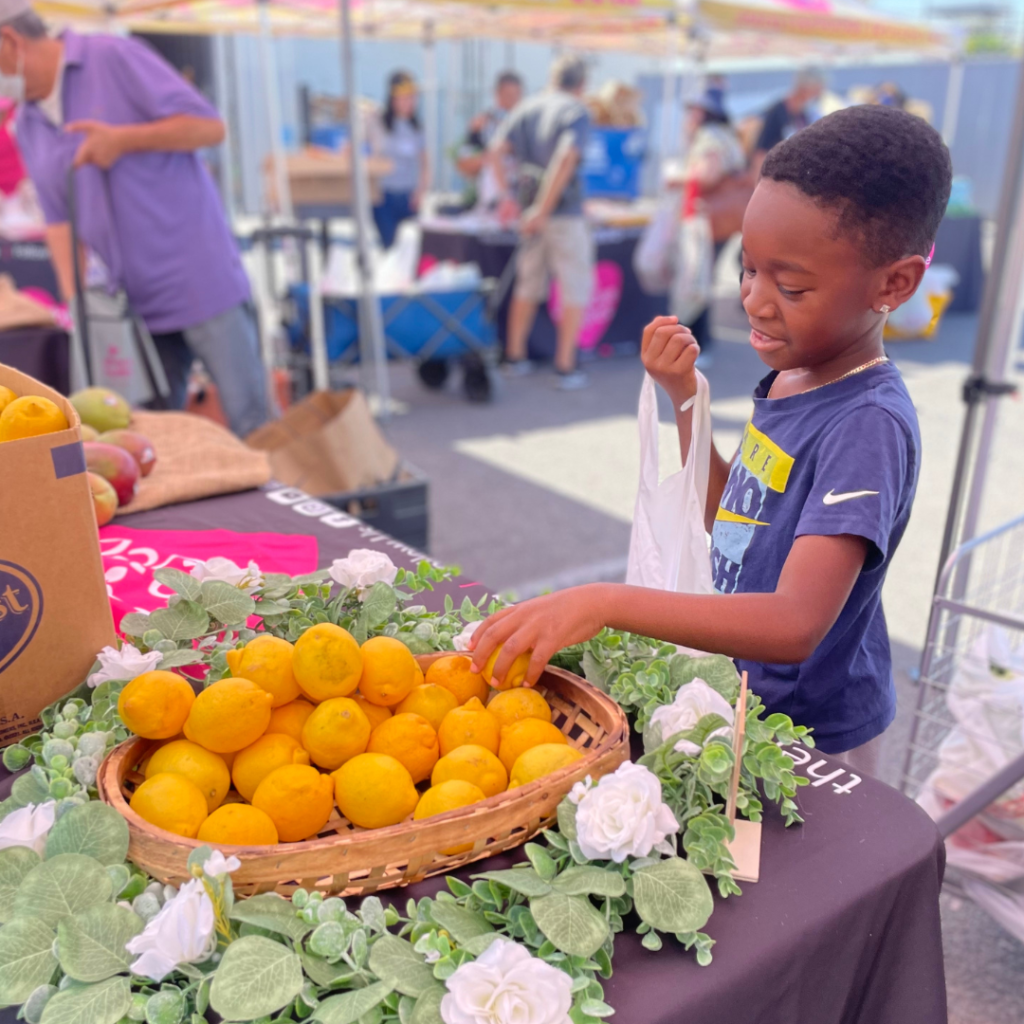 A young boy is at an outdoor market with oranges.
