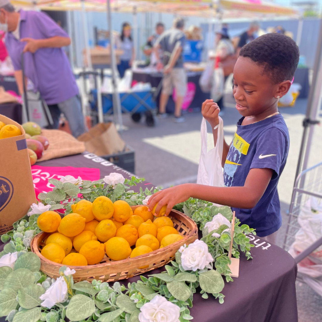A young boy is at an outdoor market with oranges.