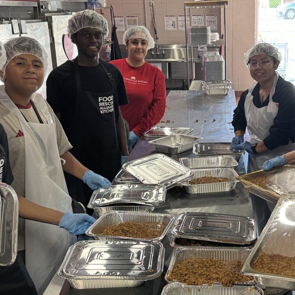 A group of people standing around trays filled with food.