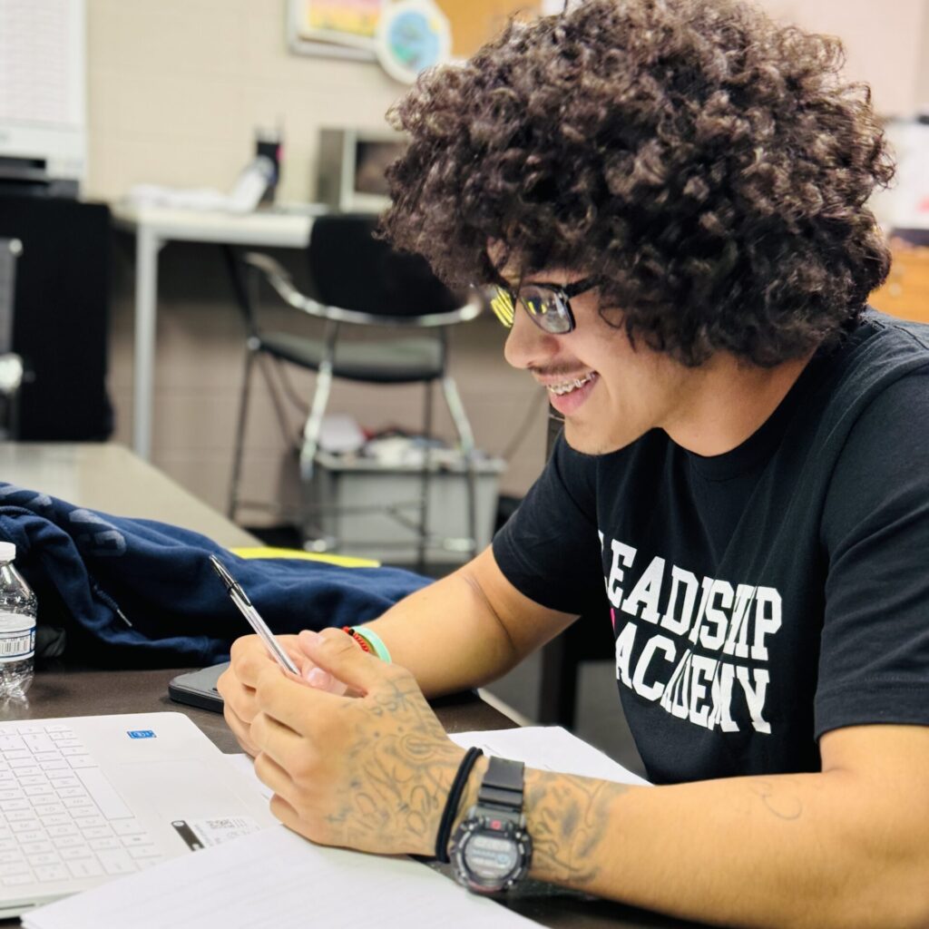 A man with curly hair is writing on paper.