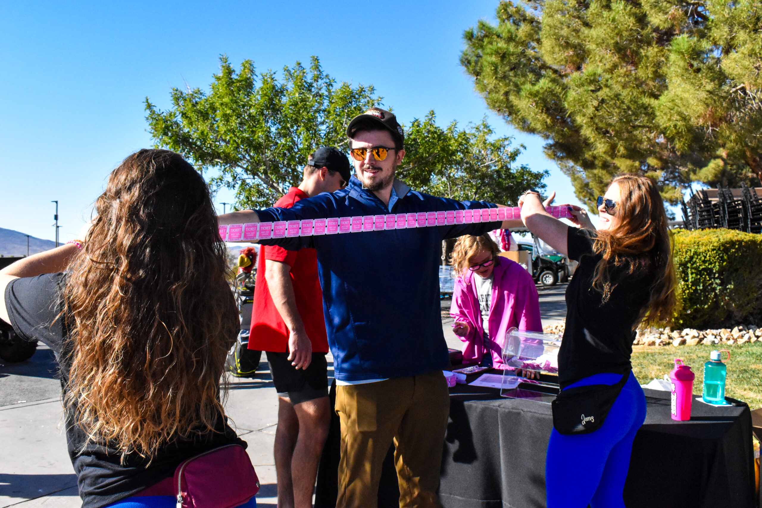 A man holding onto a pink ribbon while two women watch.