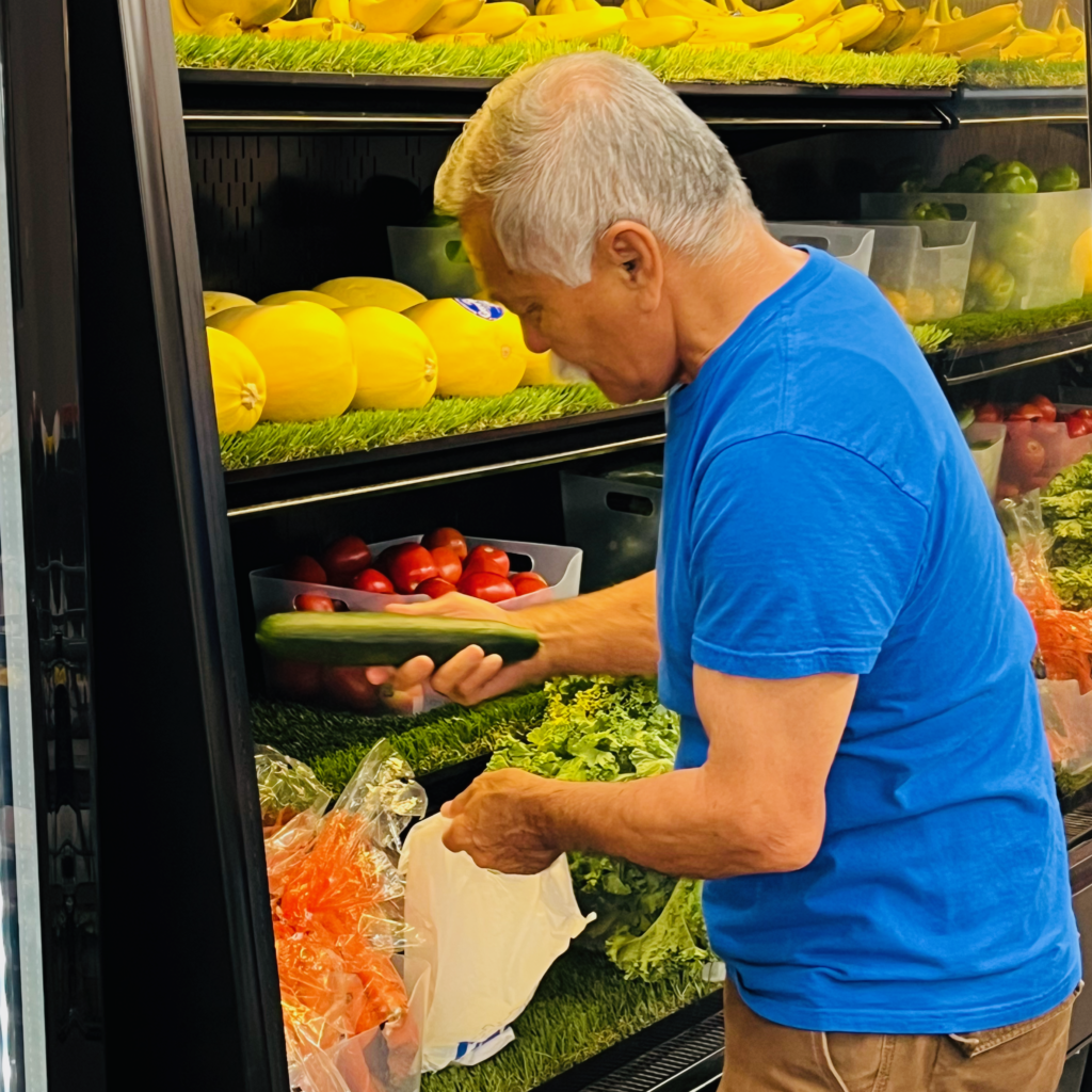 An image of a man in front of a produce cooler putting a vegetable in a bag