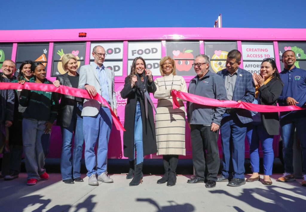A group of people standing in front of a pink food truck.