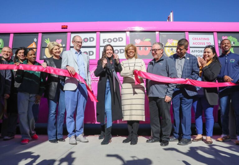 A group of people standing in front of a pink food truck.