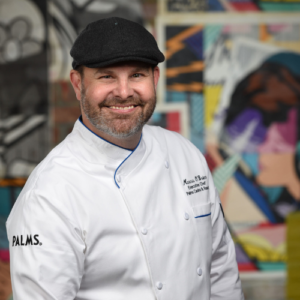 A man in chef 's outfit standing next to wall with graffiti.