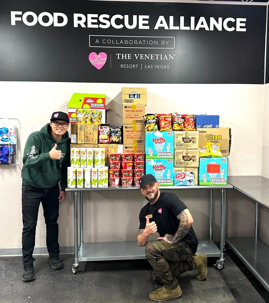 Two men standing next to a table full of food.