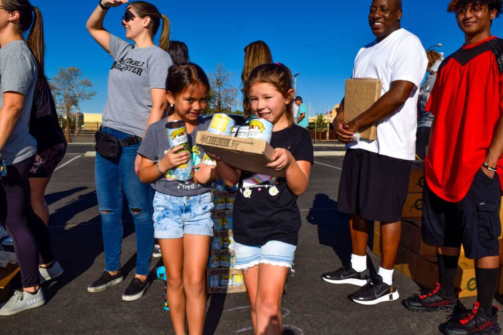 Kids and volunteers at The Just One Project mobile market carrying food donations.
