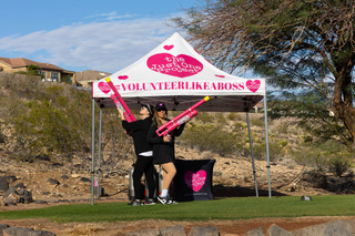 Two volunteers under The Just One Project’s #VolunteerLikeABoss canopy on the golf course hold pink air cannons, ready for a fun challenge during the 2025 Big Cup Golf Tournament.