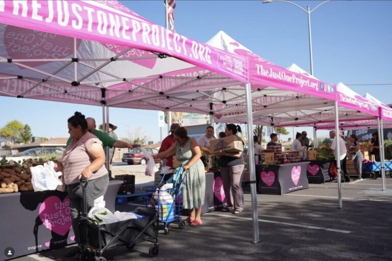 Community members receive fresh groceries at The Just One Project’s outdoor food distribution in Las Vegas, with volunteers assisting under pink tents.