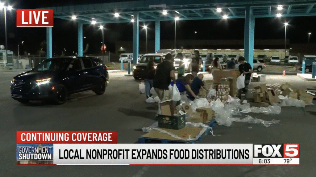 Volunteers distribute groceries late into the evening at The Just One Project’s emergency drive-thru food site in Las Vegas as cars line up under overhead lights during expanded SNAP relief services.