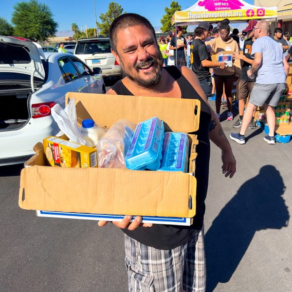 man holds up box of groceries from the just one project's pop up and give mobile market